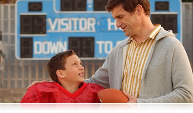 Photo of a boy in wearing football gear and his dad holding a football