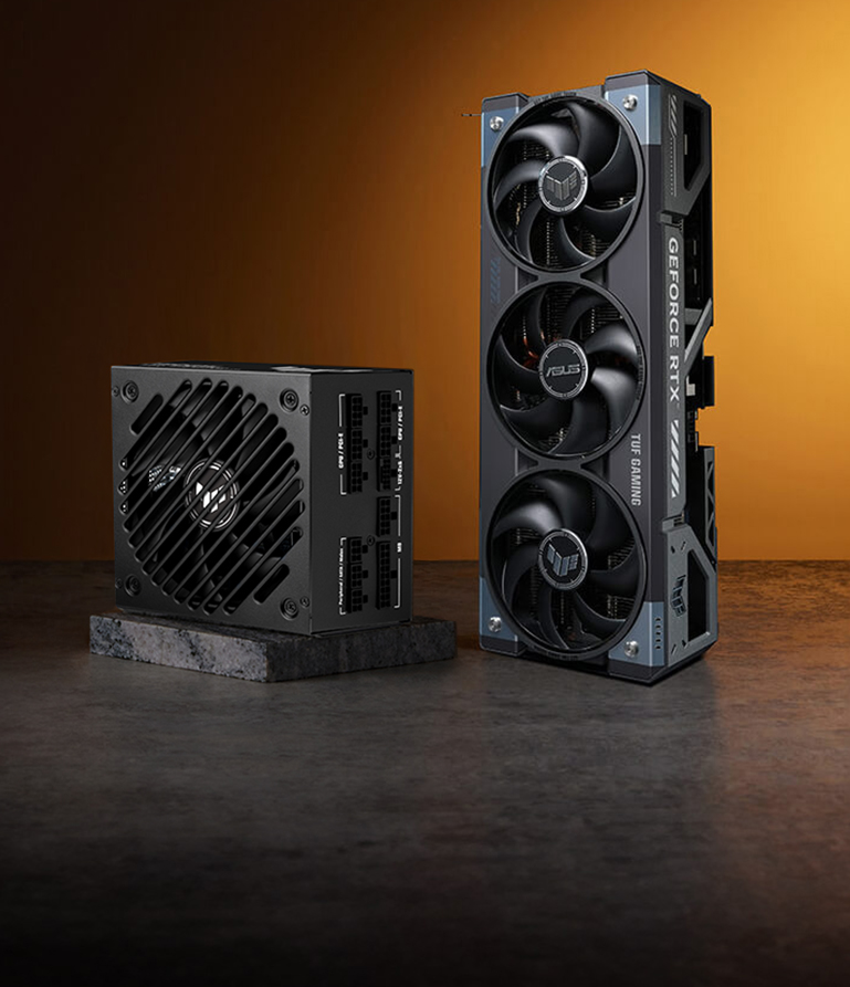 A TUF Gaming Gold EVO power supply and TUF Gaming graphics card stand on a stone surface against an orange background