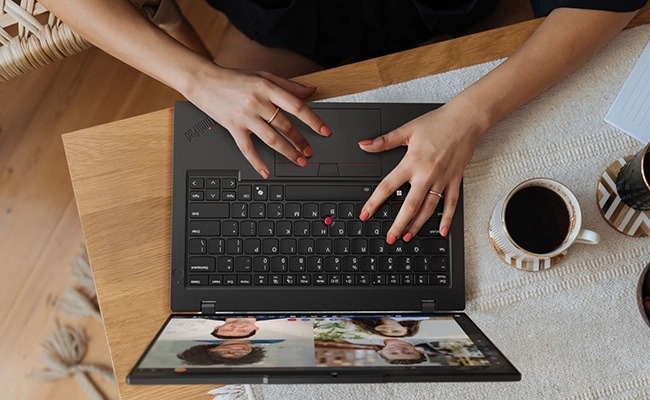 Overhead shot of a persons hands on the keyboard of a Lenovo ThinkPad L14 Gen 6 (14" AMD) laptop on a table, next to a cup of coffee